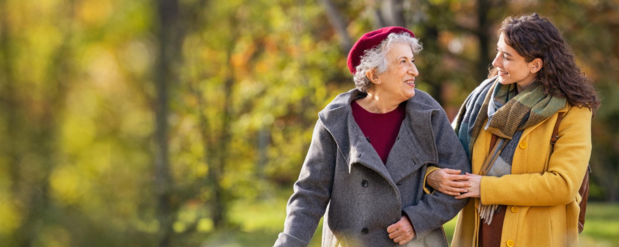 Old woman walking with a younger woman through a park in autumn